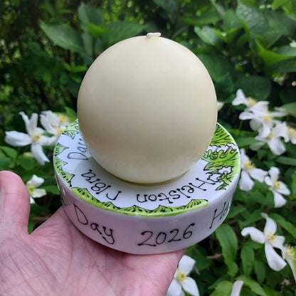 Round white candle holder with green and white lily of the valley in a hand with a floral background