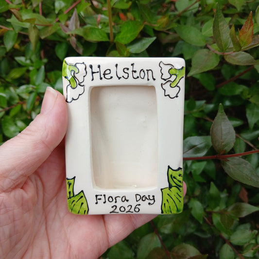 Hand holding a small square frame with decorative border against a green leafy background