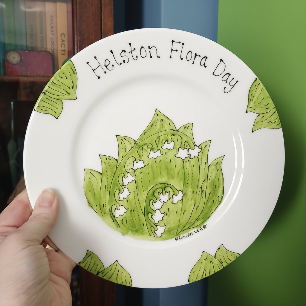White plate with green floral design and text held by a hand against a blurred background