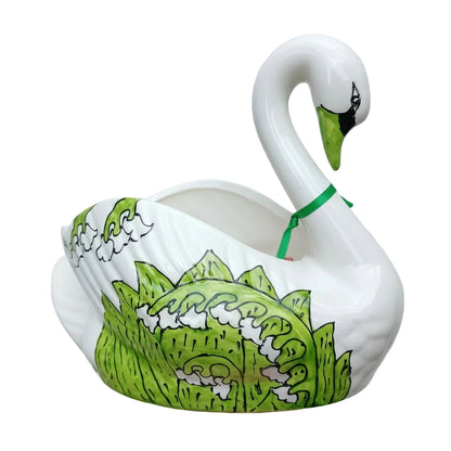 White swan-shaped container with green lily of the valley held in front of green foliage
