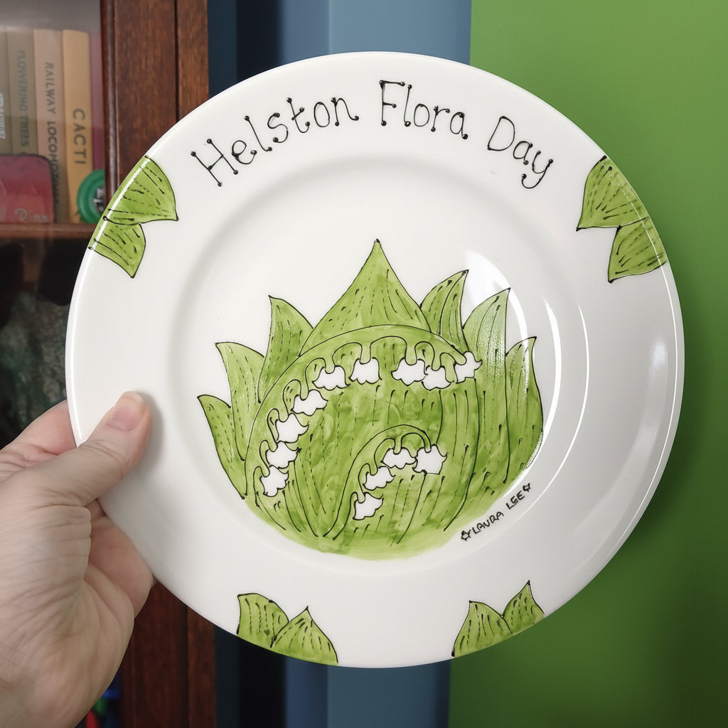 Handmade ceramic plate with green floral design and text, held against a blurred background.