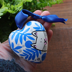 white cat surrounded by blue ferns and plants hand painted ceramic heart by Laura Lee Designs 